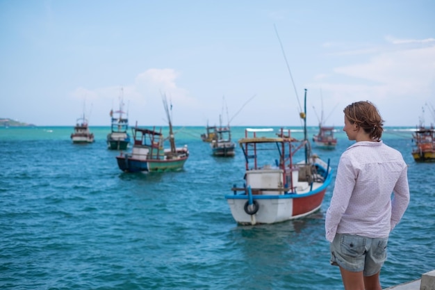 Donna caucasica in piedi sulla spiaggia di Midigama e guardando l'oceano e le tradizionali barche locali colorate