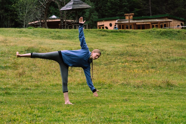 Donna caucasica in una foresta che pratica lo stretching, sullo sfondo una capanna. Concetto di relax.