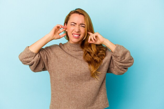 Donna caucasica isolata su sfondo blu che copre le orecchie con le dita, stressata e disperata da un ambiente rumoroso.