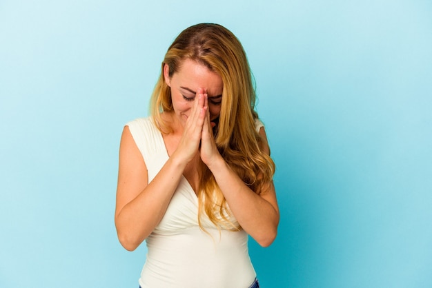 Donna caucasica isolata su sfondo blu che prega, mostra devozione, persona religiosa in cerca di ispirazione divina.