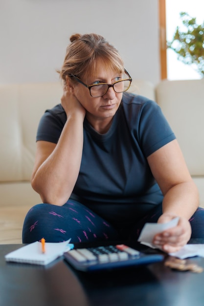 Donna caucasica preoccupata e disperata che calcola le spese monetarie domestiche facendo scartoffie e fatture bancarie contabili con calcolatrice che soffre di stress in problemi finanziari e depressione