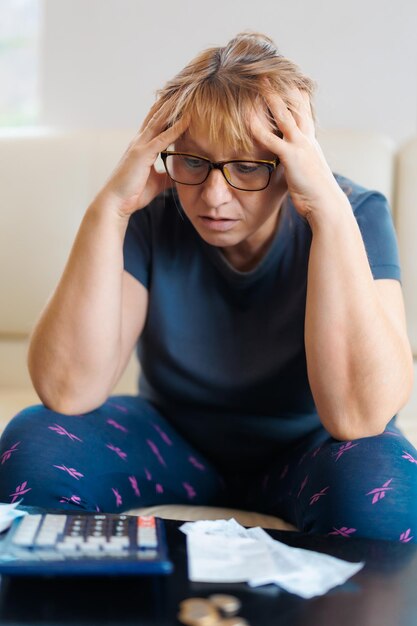 Donna caucasica preoccupata e disperata che calcola le spese monetarie domestiche facendo scartoffie e fatture bancarie contabili con calcolatrice che soffre di stress in problemi finanziari e depressione