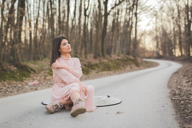 Donna caucasica seduta su un riflettore di folio sulla strada circondata da alberi senza foglie