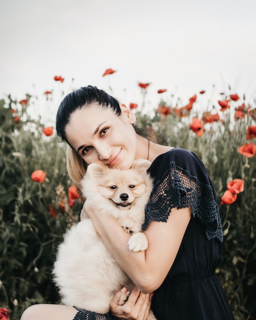 Donna che abbraccia cucciolo di Pomerania su uno sfondo di campo di fiori