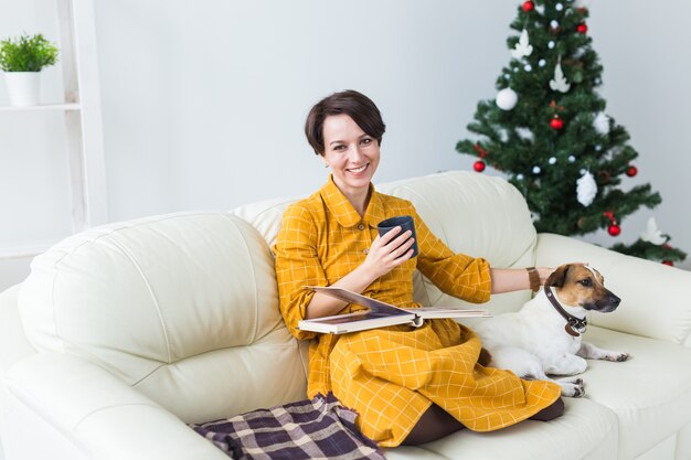 Donna che accarezza il suo cane sul divano accanto all'albero di Natale