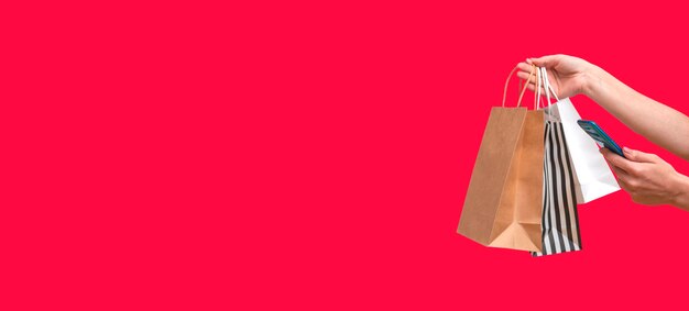 Donna che acquista online da un telefono cellulare. Mani femminili con pacchetti isolati su sfondo rosso, copia dello spazio. Banner