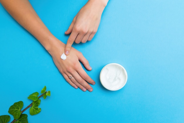 Donna che applica crema idratante bianca sulle sue mani con sfondo blu