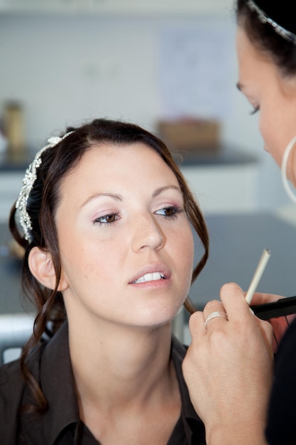 Donna che applica il trucco per una sposa nel giorno delle nozze vicino allo specchio