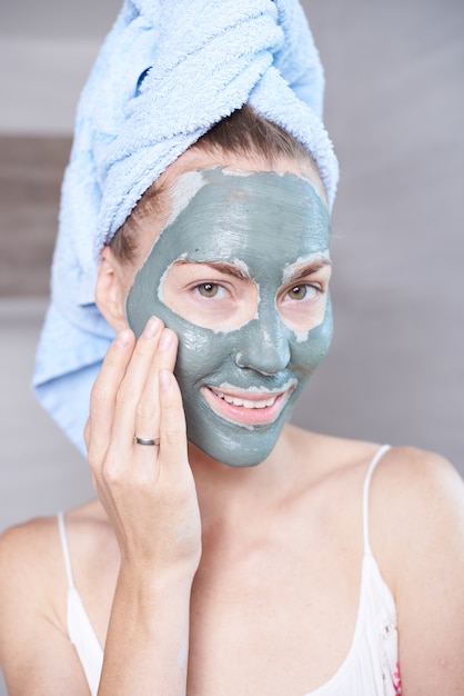 Donna che applica la maschera idratante crema per la pelle sul viso guardando nello specchio del bagno. Ragazza che si prende cura della sua crema idratante a strati di carnagione. Trattamento spa per la cura della pelle.