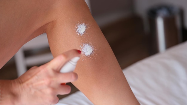 Donna che applica lo spray idratante sulle gambe nella camera da letto di casa