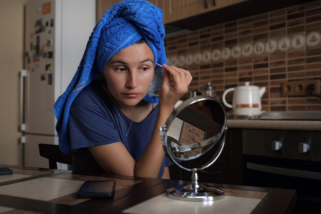 Donna che applica make up prodotto di bellezza con specchio per il trucco rotondo nella cucina di casa