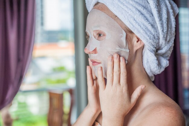 donna che applica un foglio maschera facciale