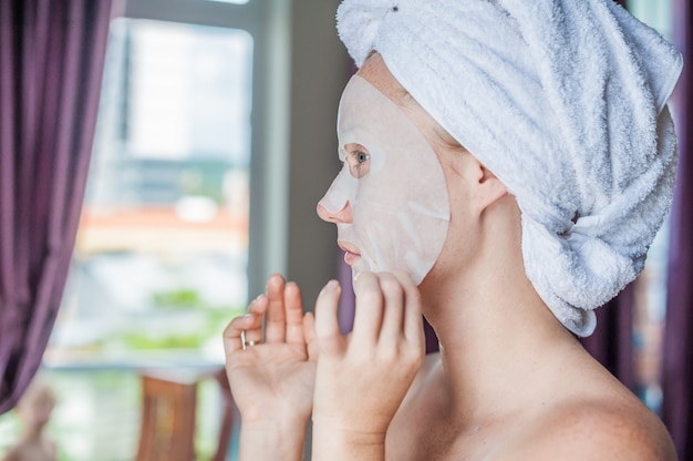 donna che applica un foglio maschera facciale