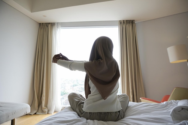 Donna che apre le tende in camera da letto al mattino per fare stretching del corpo