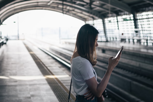 Donna che aspetta sulla piattaforma della stazione e che utilizza lo Smart Phone alla stazione di collegamento dell&#39;aeroporto