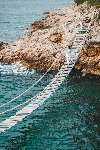 Donna che attraversa il ponte sospeso sul mare sullo sfondo