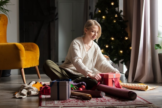 Donna che avvolge i regali di Natale a casa su un pavimento.