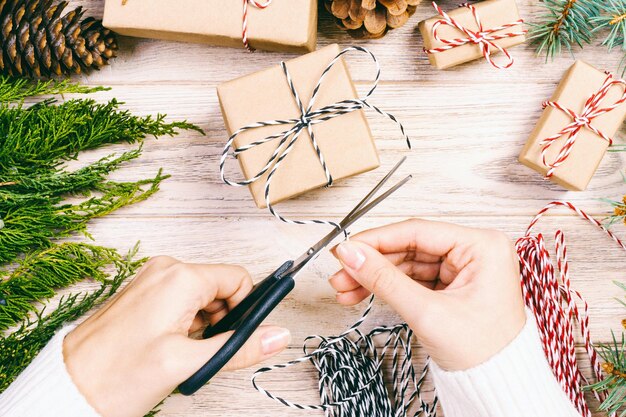 Donna che avvolge il regalo di Natale Ragazza che prepara i regali di Natale con abete e cono di pino Regalo fatto a mano su sfondo di legno con decorazione natalizia Top view copy space Toned