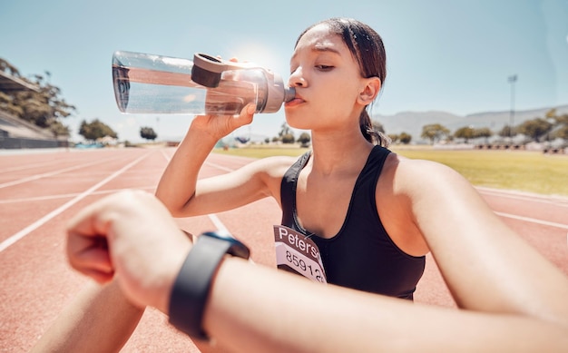 Donna che beve acqua o controlla l'orologio intelligente durante l'allenamento in pista o durante l'allenamento Atleta sportivo corridore o persona di fitness con salute smartwatch o tracker del tempo per la salute o la velocità