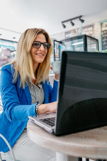 Donna che beve caffè e lavora con il laptop in una caffetteria