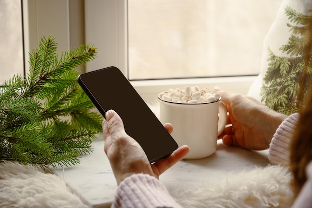 Donna che beve caffè e lavora nello smartphone accogliente vacanza invernale