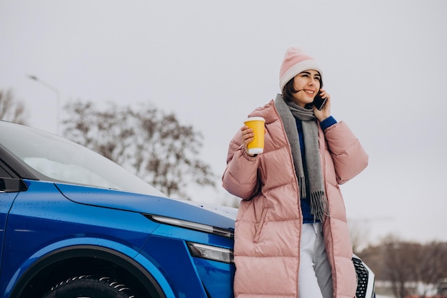 Donna che beve caffè e parla al telefono con la sua auto in inverno