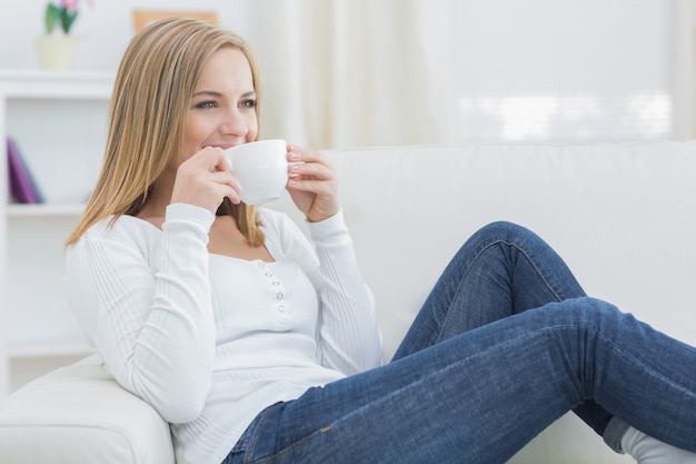 Donna che beve caffè mentre guarda lontano sul divano