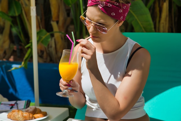 Donna che beve il succo con una cannuccia mentre è seduto su un lettino