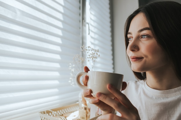 Donna che beve il tè, seduto alla finestra in una mattina di sole. Riposo a casa.