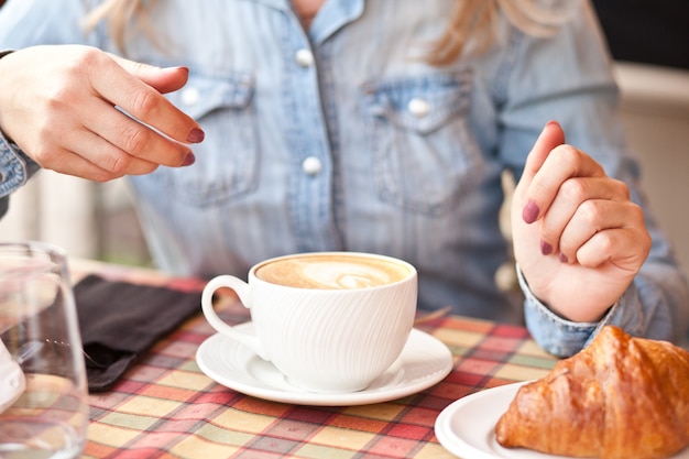 Donna che beve un caffè con croissant in una terrazza di un bar cafe