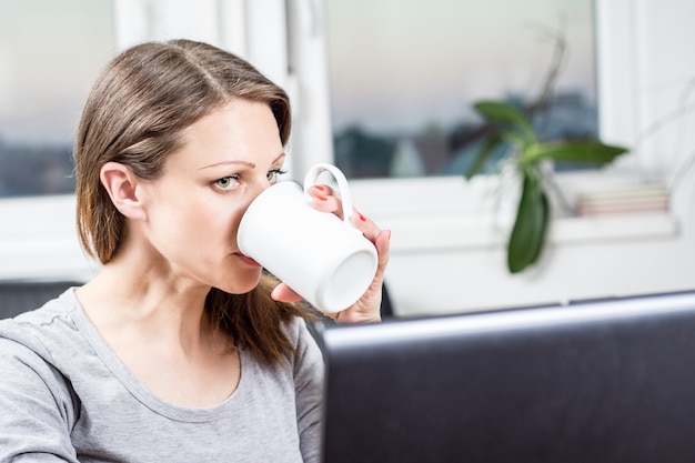 donna che beve un caffè e lavora al computer portatile
