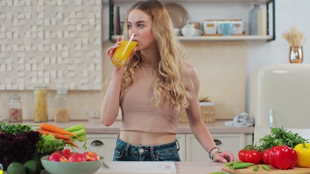 Donna che beve un succo d'arancia in cucina Attraente ragazza sportiva che beve succo fresco Stile di vita e concetto di nutrizione sana