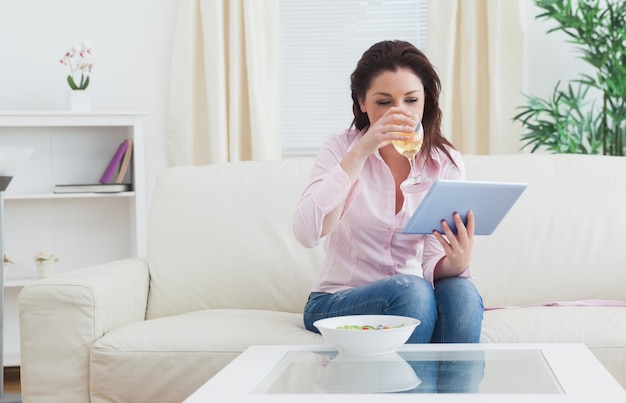 Donna che beve vino mentre si utilizza la tavoletta digitale a casa