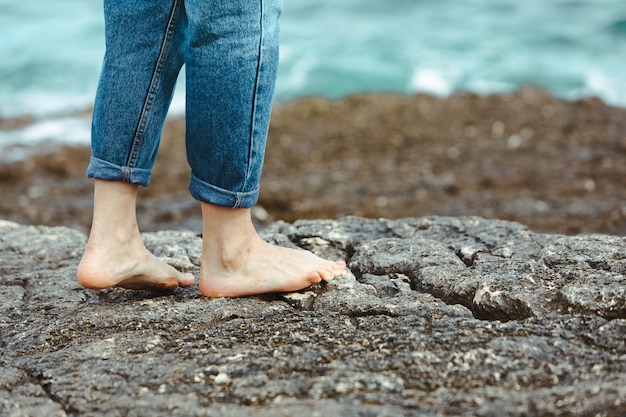 Donna che cammina a piedi nudi in riva al mare tenendosi per mano scarpe bianche vacanze estive