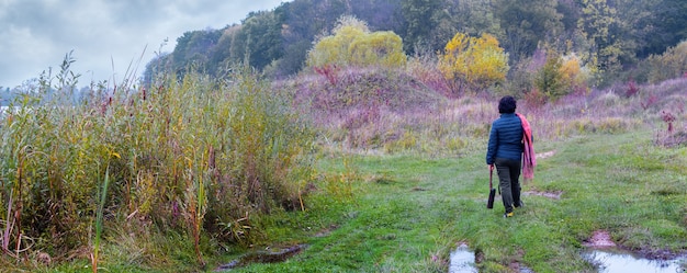 Donna che cammina allo stato brado vicino al fiume e alla foresta in un tempo nuvoloso autunnale