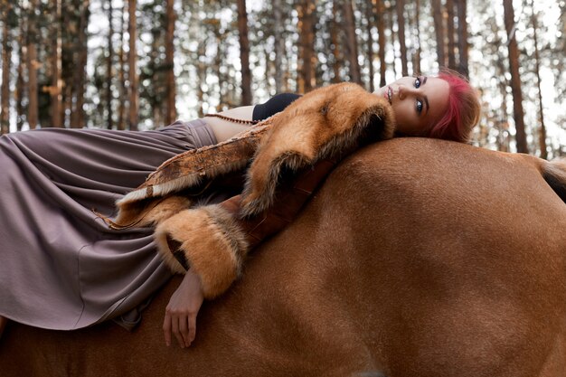 Donna che cammina con l'autunno del cavallo sulla natura. Volto di donna trucco rosa caldo creativo, colorazione dei capelli. Ritratto di una donna con un cavallo. Equitazione nella foresta d'autunno. Vestiti autunnali