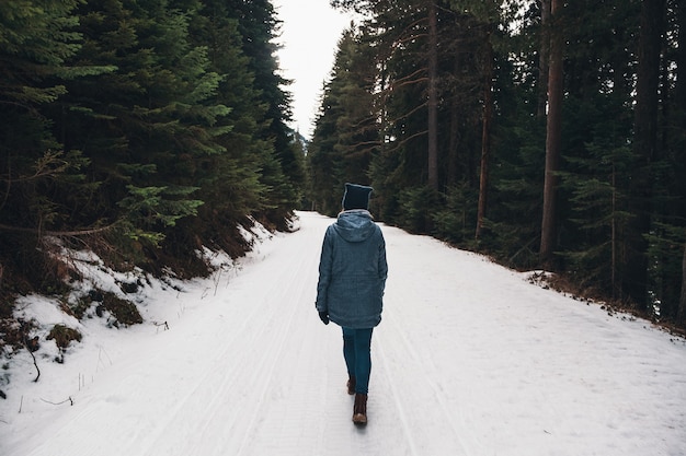 Donna che cammina in una foresta invernale. Avventuriero, cammina tra enormi pini su una strada innevata. Fantastico viaggio nel deserto invernale. Vista posteriore.