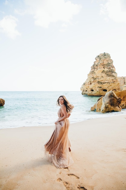 Donna che cammina lungo la spiaggia contro le rocce e l'oceano