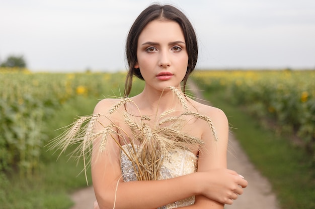 Donna che cammina nel campo di erba secca dorata. Bellezza naturale del ritratto. Bella ragazza che tiene il raccolto di grano nelle sue mani mentre si trova nel campo di grano giallo