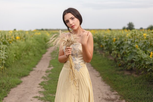 Donna che cammina nel campo di erba secca dorata. Bellezza naturale del ritratto. Bella ragazza che tiene il raccolto di grano nelle sue mani mentre si trova nel campo di grano giallo