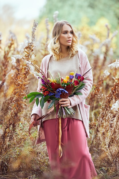 donna che cammina nella foresta di autunno. Un grande bellissimo mazzo di fiori nelle mani di una donna. la donna sta in erba rossa gialla, natura di autunno