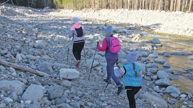 Donna che cammina nella natura vicino al fiume di montagna Ragazze e bambini usano bastoncini da trekking e bastoncini nordici