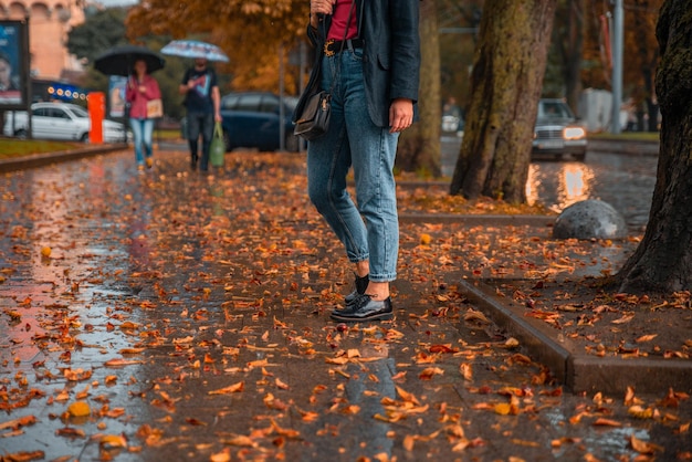 Donna che cammina per strade bagnate dopo la pioggia. foglie gialle a terra. l'autunno sta arrivando