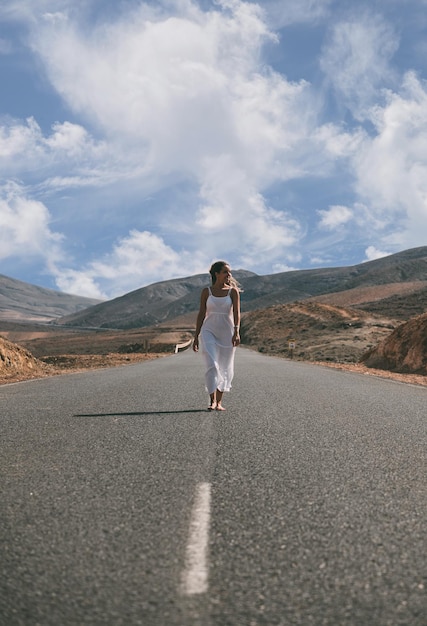 Donna che cammina sulla strada vicino alle colline sotto il cielo nuvoloso