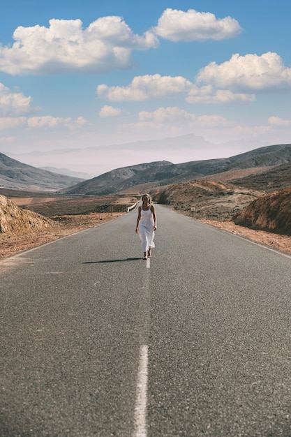 Donna che cammina sulla strada vicino alle colline sotto il cielo nuvoloso