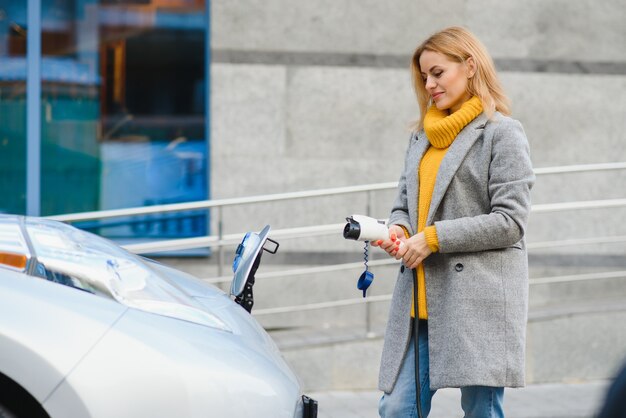 Donna che carica elettro automobile al distributore di benzina elettrico