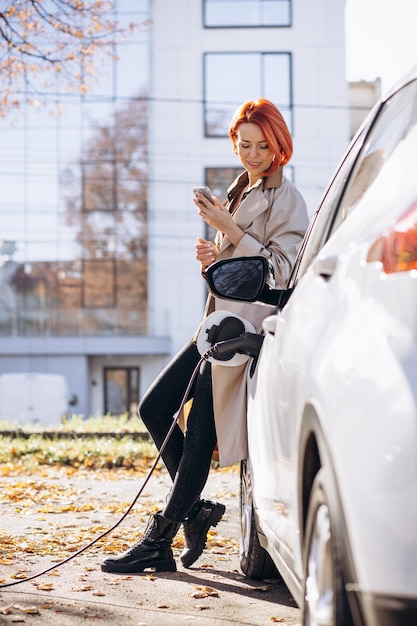 Donna che carica un'auto elettrica e utilizza il telefono