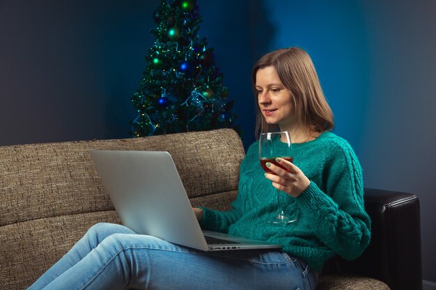 Donna che celebra la vigilia di Natale con i parenti tramite una chiamata online su un laptop bevendo vino