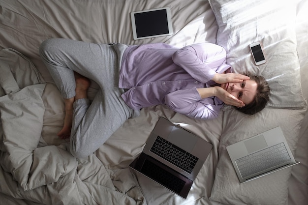 Donna che cerca di lavorare essendo malata stare a casa sul letto con il computer sul letto