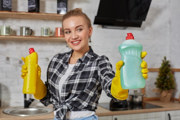 Donna che confronta i prodotti detergenti, tiene in mano due bottiglie e le controlla nella cucina di casa.